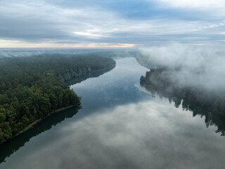 Obraz premium Aerial drone view of a lake surrounded by green forest. Big lake in the fog and clouds. Lake in the Masurian Lake District. Lake Lesk in the Kulka Reserve in Poland. Kulka Reserve, Masuria, Poland.