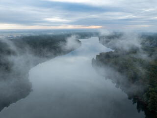 Aerial drone view of a lake surrounded by green forest. Big lake in the fog and clouds. Lake in the Masurian Lake District. Lake Lesk in the Kulka Reserve in Poland. Kulka Reserve, Masuria, Poland.
