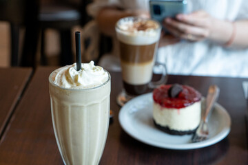 Deliciosa merienda de capuchino helado y cheesecake de frutos rojos. Persona usando el celular de fondo