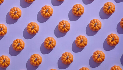 A creative arrangement of small orange pumpkins on a soft pastel purple background. Perfect for autumn and Halloween themes, the pattern evokes a festive and cozy atmosphere.