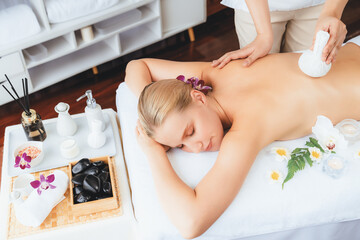 Hot herbal ball spa massage body treatment, masseur gently compresses herb bag on woman body....