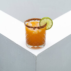 Photo of an Extremely Low Angle Shot From Floor Level of Short Glass Filled With Orange Juice and Ice, With Tajin Rim and Lime Wheel.