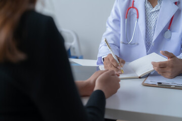 Doctor with a stethoscope takes notes while consulting a patient in a hospital office, emphasizing...