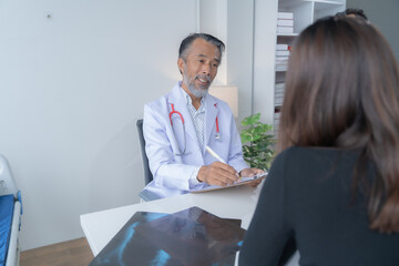 Obraz premium Senior male doctor is explaining a diagnosis to a female patient, writing notes on a clipboard during a medical consultation