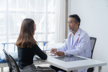 Senior doctor consults with a female patient in a hospital room, discussing health and treatment with care and professionalism