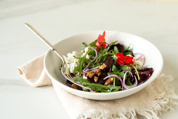 white bowl with salad with beetroot, ricotta and nuts on light table