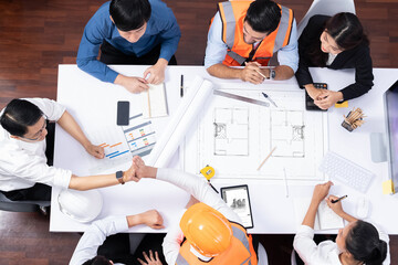 Top view banner of diverse group of civil engineer and client working together on architectural project, reviewing construction plan and building blueprint at meeting table. Prudent