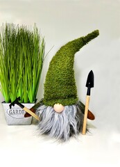 Gnome in green cap with gardening tools near flowerpot with grass 
