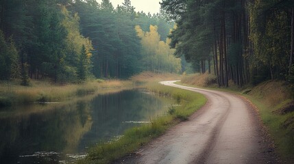 Obraz premium A serene path winding alongside a tranquil river, lined with lush trees, creating a peaceful nature scene.