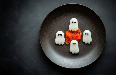  black plate with Halloween-themed food on it, a fork and knife beside the dish, a dark grey background.Minimal creative holiday food concept.Flat lay