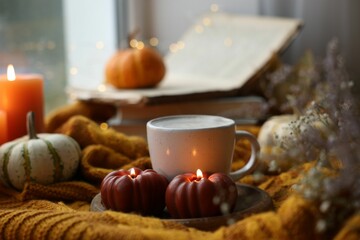 Cup of coffee and burning pumpkin shaped candles on soft sweater. Autumn atmosphere