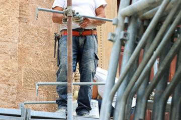 Worker with tools tied to his jeans belt works on a construction site