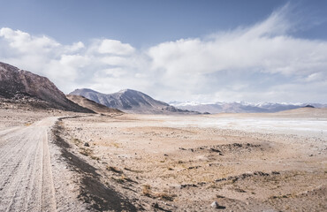 Dusty road of the Pamir Highway winds and twists in the valley of the Tien Shan mountains in Tajikistan in Pamir, landscape in the high desert mountains for background