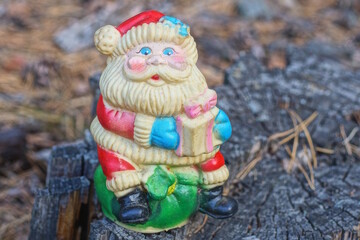 one plastic colored santa claus toy stands on a gray wooden stump in nature