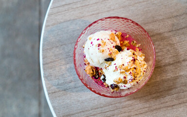Vanilla ice cream with nuts and raisins in pink bowl on wooden table. Two scoops, ice cream dessert. Overhead shot.