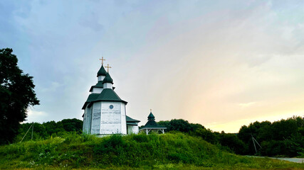 Fototapeta premium A wooden Orthodox church in the Cossack Baroque style, situated on a grassy hill in the village of Hryhorivka, Cherkasy region, Ukraine, during sunset.