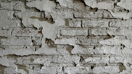 A close-up of a weathered brick wall with peeling white paint, showcasing the rough texture and aged appearance of the surface.