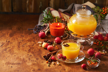 Glass teapot and cup with sea buckthorn tea with spices and autumn small crabapples on wooden background