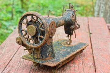 one old discarded black industrial retro iron rusty historical dirty broken manual heavy sewing machine stands on brown wooden table daytime outdoors