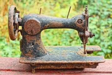 one old discarded black industrial retro iron rusty historical dirty broken manual heavy sewing machine stands on brown wooden table daytime outdoors