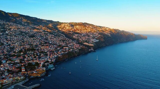 Densely populated slopes of the mountains on the coast of the North Atlantic Ocean. Some yacht sail at the shore of the Madeira Islands, Portugal. Aerial view.