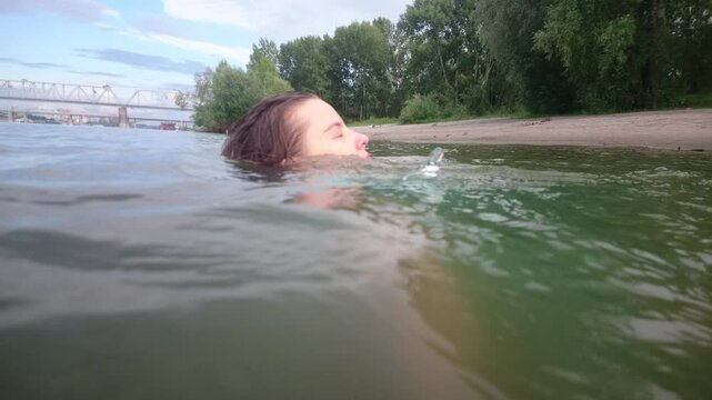 Attractive girl have fun, dives and drowned at the urban beach in the water. Woman portrait with blue dress. 