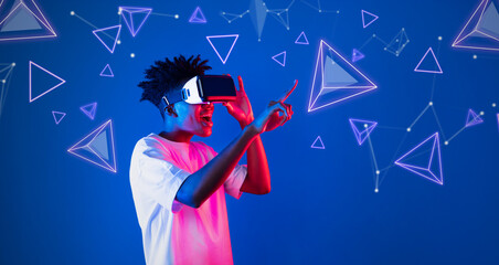 Smart boy standing at blue background while floating geometric shape. African man playing game and wearing VR goggle and casual shirt. Augmented reality technology innovation concept. Ingenuity.