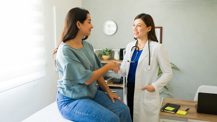 Female doctor smiling and shaking hands with her hispanic patient after a consultation in her office