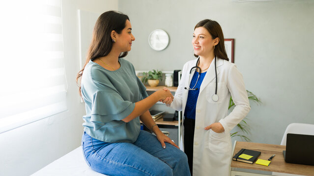 Female doctor smiling and shaking hands with her hispanic patient after a consultation in her office