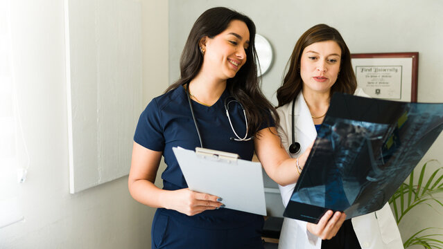 Cheerful doctor and a nurse review an x-ray image of a patient's spinal column in a medical clinic