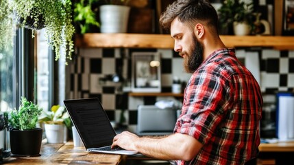 A young man types on his laptop at a cafГ© filled with plants and wooden decor, focused on his work while enjoying the relaxed atmosphere in the afternoon light