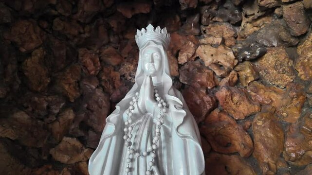 4k low angle video footage of A large white statue of Mary made of stone carvings in grottoes with flowers and candles lit decoration.