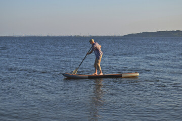 Naklejka premium An elderly man pours on SUP while standing.