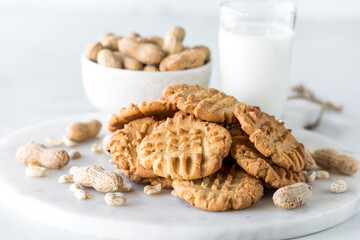 A pile of fresh homemade peanut butter cookies surrounded by peanuts.