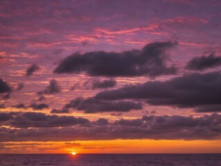 Obraz premium A colorful sunset sky over the ocean, with streaks of purple, pink, and gold blending together as the sun dips below the horizon 