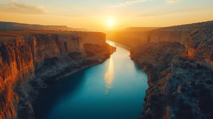 A scenic view of a river canyon at sunset. The sun is setting behind the canyon walls, casting a golden glow over the water.