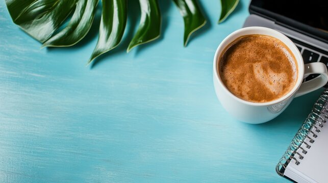 A steaming cup of coffee is placed next to a laptop and a spiral notebook on a light blue desk, embodying creativity and focus in a cozy, inviting workspace.