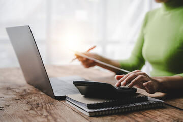Fototapeta premium Close-up of young woman's hand working with tax and accounting documents using laptop and calculator to calculate financial transactions, taxes, company income. Finance and tax concepts