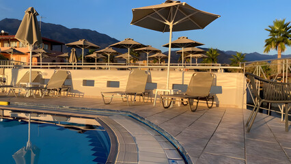 Fototapeta premium Sun loungers with umbrellas illuminated by the sun at sunset near the pool beach sea mountain palm trees