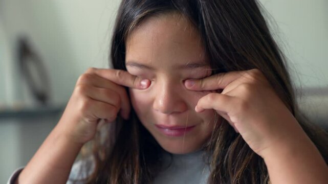 Young girl rubbing her eyes with both hands, showing signs of tiredness. A relatable moment reflecting childhood exhaustion and the need for rest