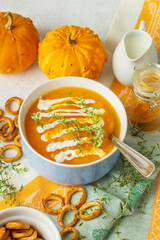 Pumpkin soup puree with sauce in bowl  with whole pumpkins, thyme, cream, turmeric and salty rings  for the cooking recipe