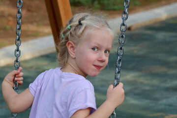 Little blonde girl. Little girl, toddler swinging on a swing in the park. Portrait of a girl, toddler.