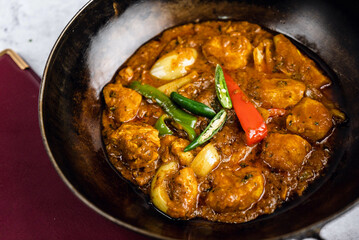 Spicy chicken curry served in a dark stone bowl, with chicken pieces in a vibrant, aromatic sauce, garnished with green and red chilies and onion chunks.
