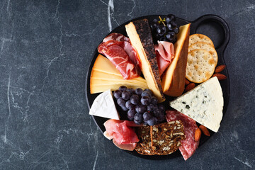 Charcuterie board of a selection of cheeses, meats and appetizers. Overhead view on a dark...