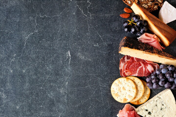 Selection of charcuterie cheeses, meats and appetizers. Top down view side border on a dark black stone background with copy space.