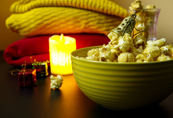 Popcorn bowl with golden bell on top and blurred Christmas decorations at the back. Close-up popcorn decor with bell in dark. Concepts of snack for party at night, candle, Xmas, and romantic in winter