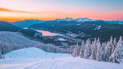 A panoramic view of a snow-covered mountain range with a lake and town in the distance during a beautiful sunset.