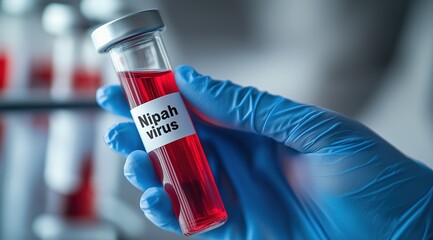 Nipah virus. A gloved hand holds a test tube labeled "Nipah virus" with virus cells blurred in the background.