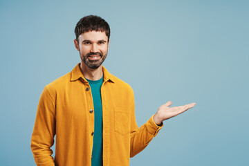 Portrait of middle aged Latin man wearing stylish yellow shirt showing with hand, looking at camera