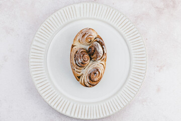 A gourmet cinnamon roll elegantly arranged on a textured white plate, showcasing its swirled pattern and freshly baked appearance, perfect for dessert.